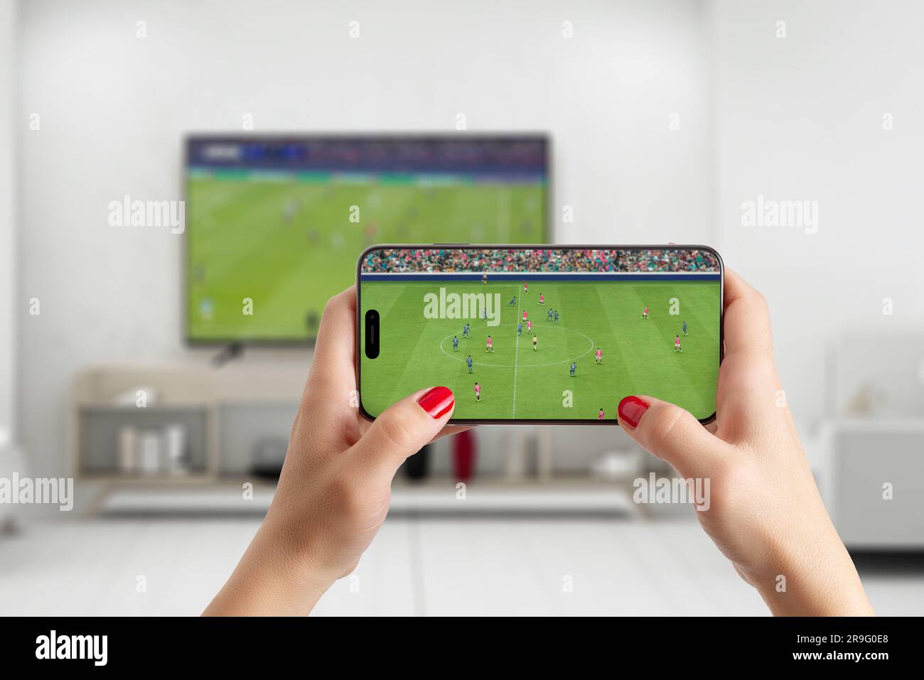 Watching soccer game on smart phone and tv in living room. Phone in woman hand in horizontal position Stock Photo