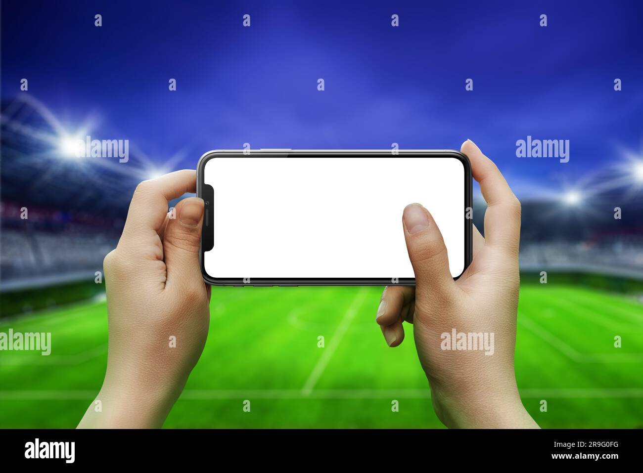 Phone in hands, horizontal position. Isolated screen for mockup. Soccer stadium in background Stock Photo