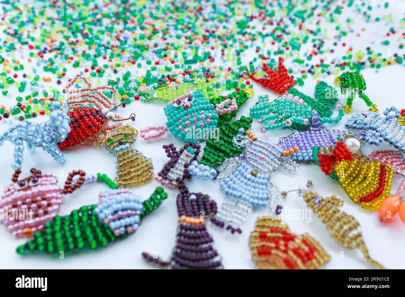 Small multi-colored beads on a white background. Small colored figurines of plants and animals woven from beads. Stock Photo