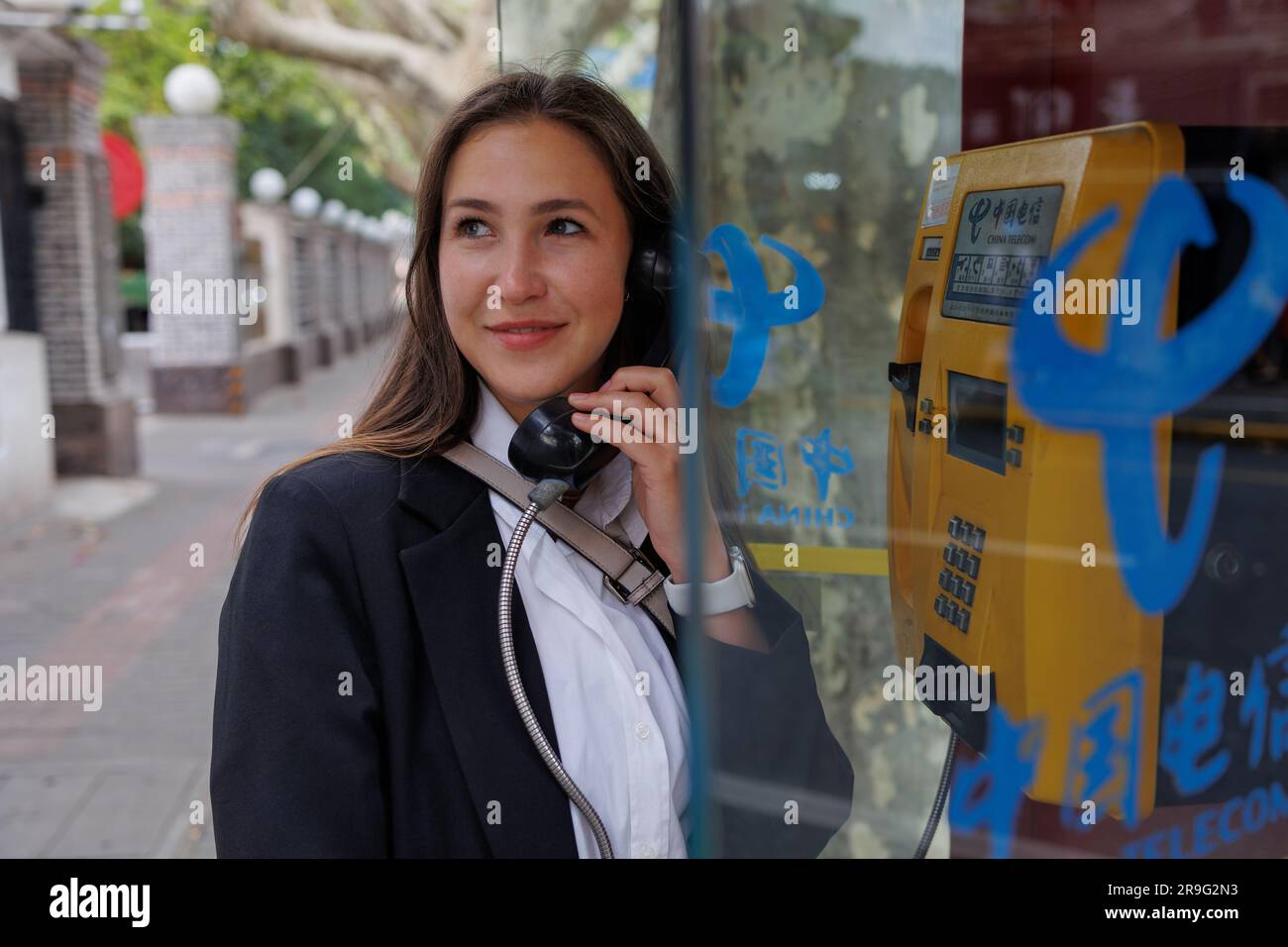 Young smiling woman in black jacket calling with city call box in Shanghai. Stock Photo