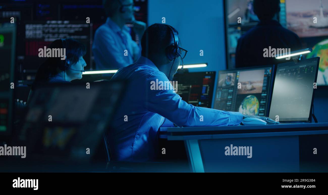 African American flight control employee monitors space mission on multi-monitor computer in mission control center. Team watch successful spacecraft lift off on big digital screen. Space exploration. Stock Photo