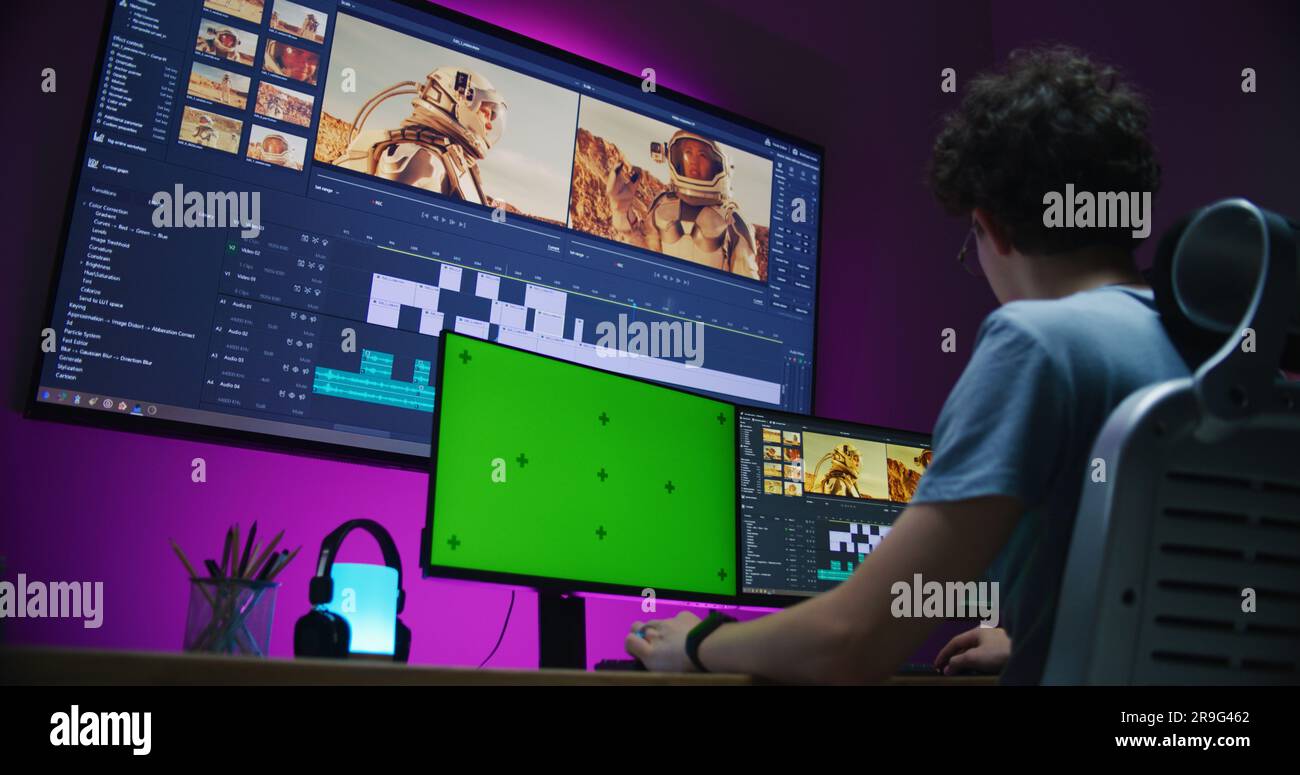 Young video maker edits movie about space mission, works at home office. Film footage and software interface with tools and sound tracks on big digital screen. Computer monitor with green screen. Stock Photo