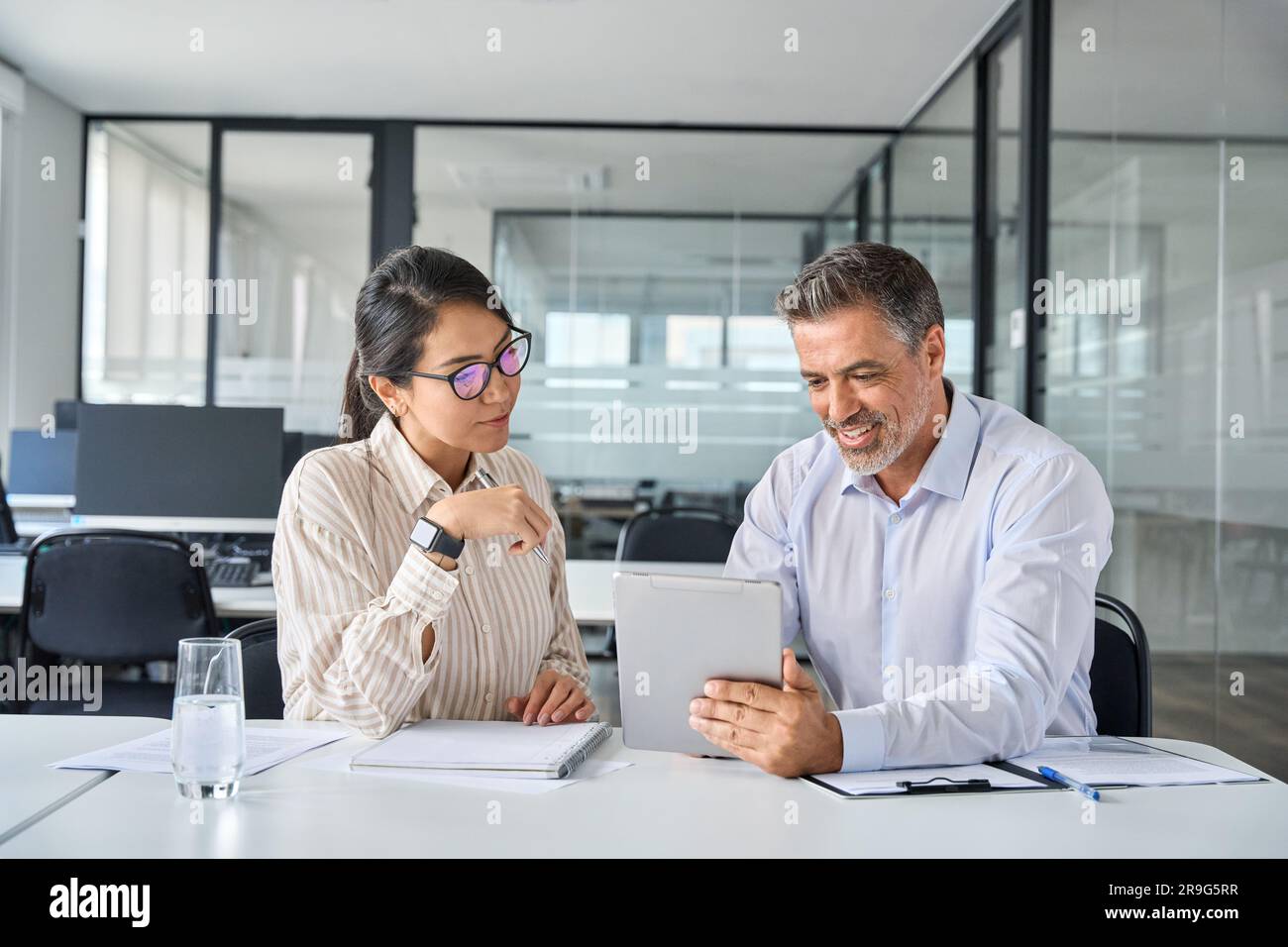 Two busy diverse executives team discussing work using digital tablet in office. Stock Photo