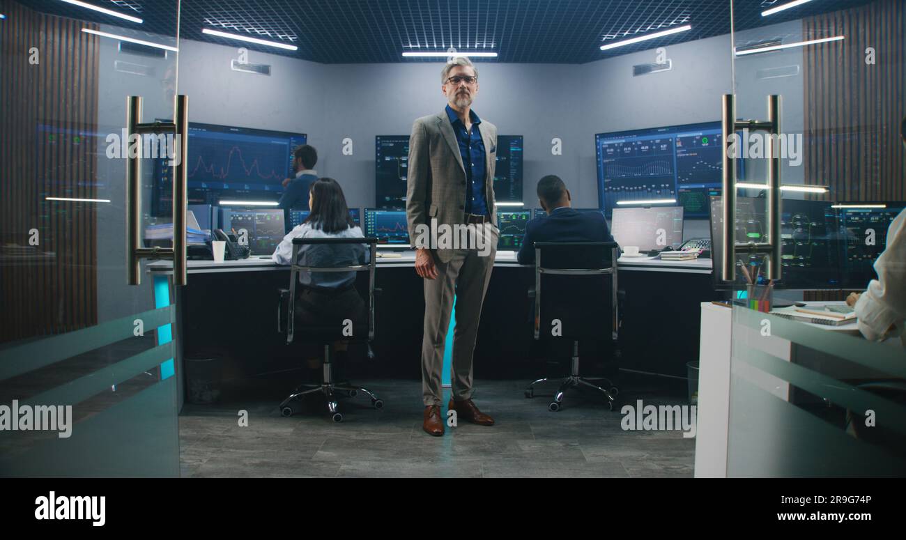 Giant Using Computer Mature big data scientist puts on glasses, stands in monitoring room ...
