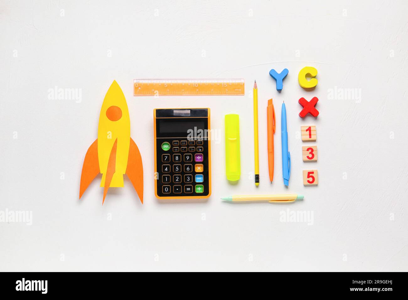 Yellow paper rocket with calculator, pens and ruler on white background ...