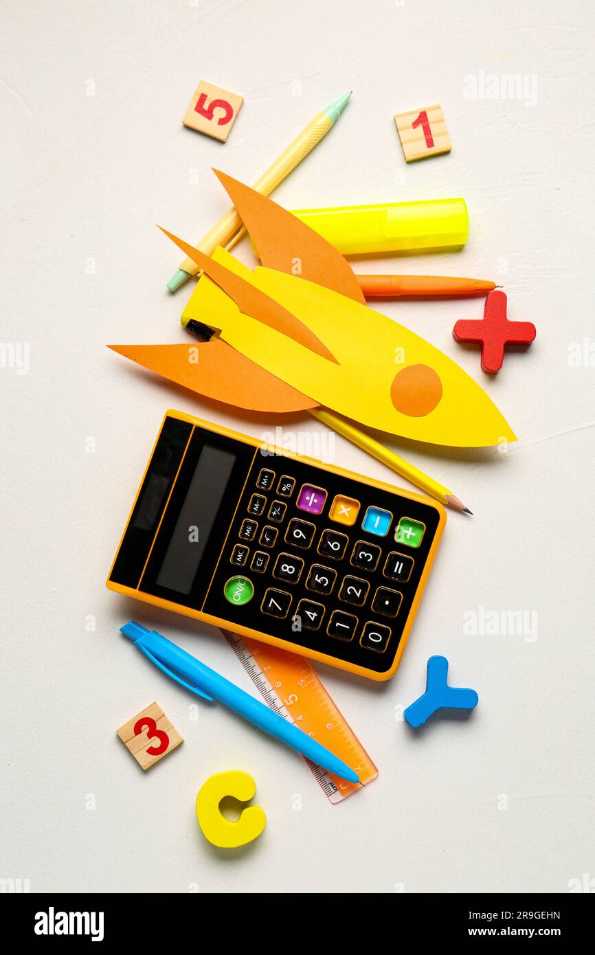 Yellow paper rocket with calculator, pens and ruler on white background ...