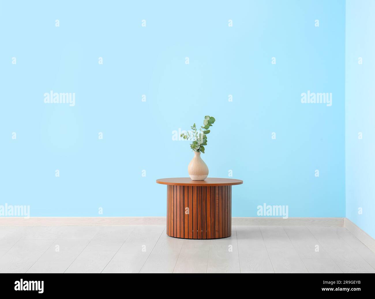 Wooden coffee table with eucalyptus branches in vase near blue wall ...