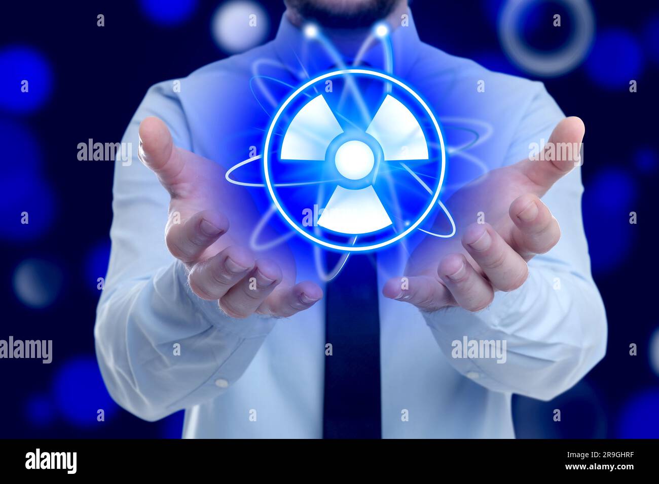 Man holding atom symbol with radiation warning sign on dark blue background, closeup. Bokeh effect Stock Photo