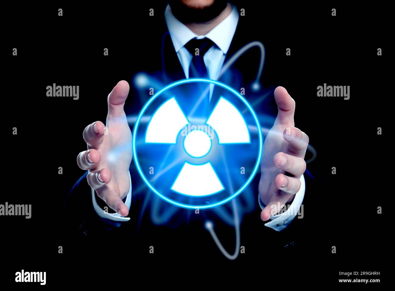 Man holding glowing atom symbol with radiation warning sign on black background, closeup Stock Photo