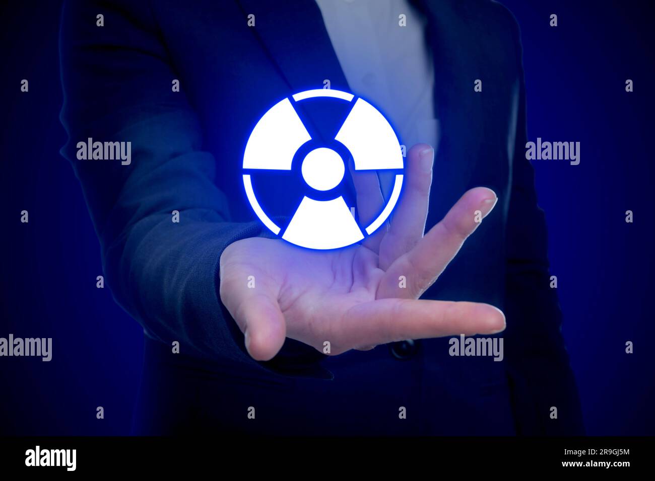 Woman holding glowing radiation warning symbol on dark blue background, closeup Stock Photo