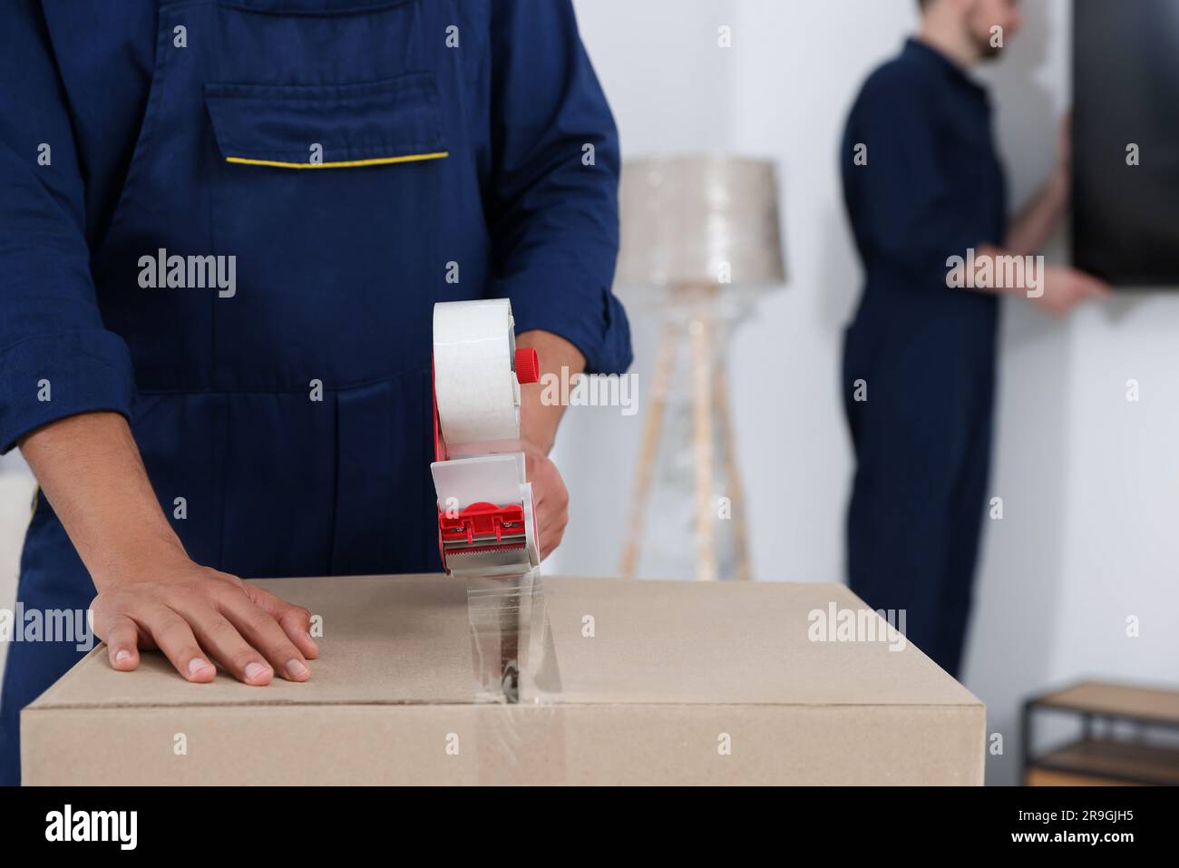 Male mover packing box with adhesive tape in house, closeup. Space for