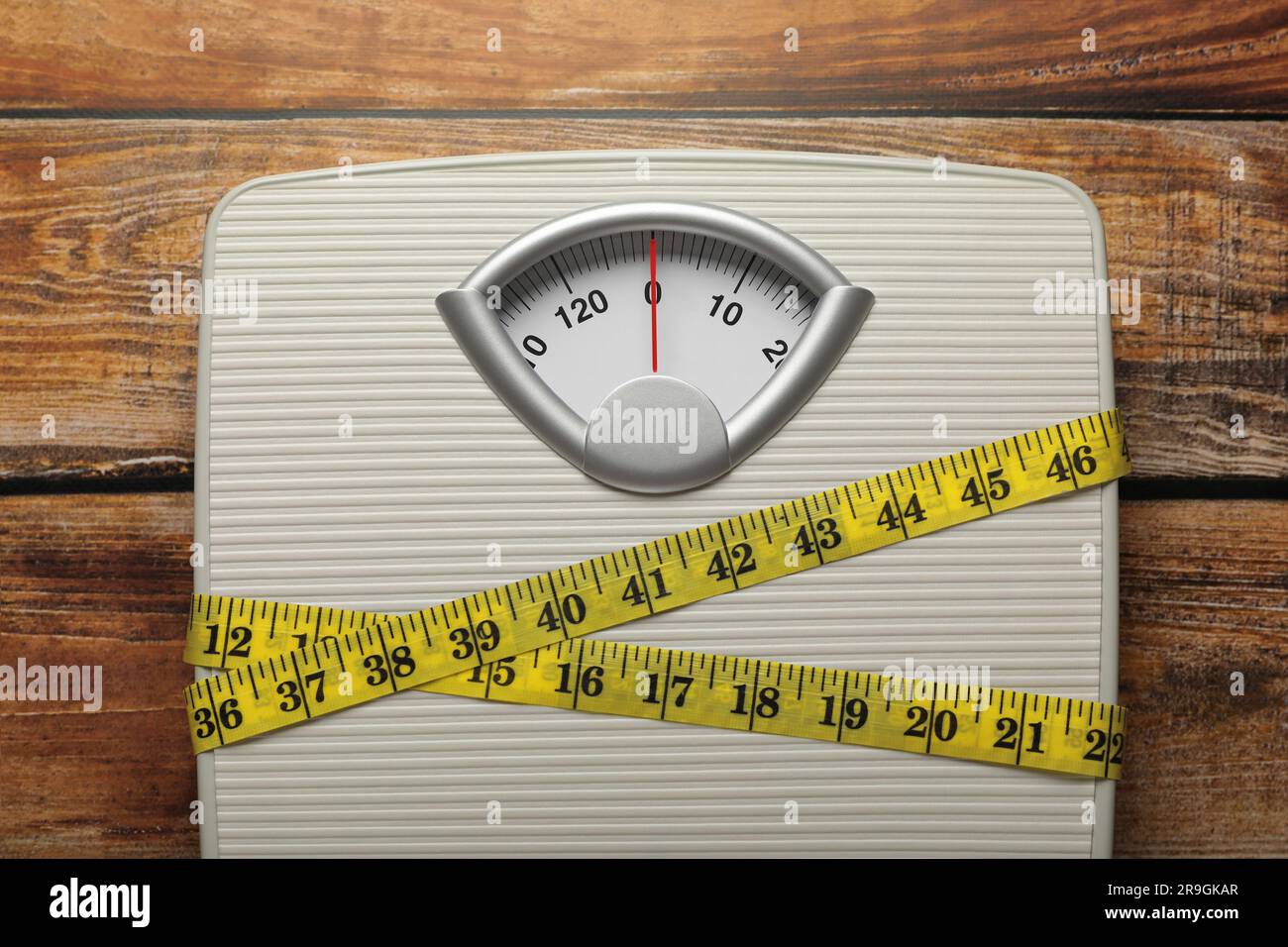 Weigh scales tied with measuring tape on wooden table, top view