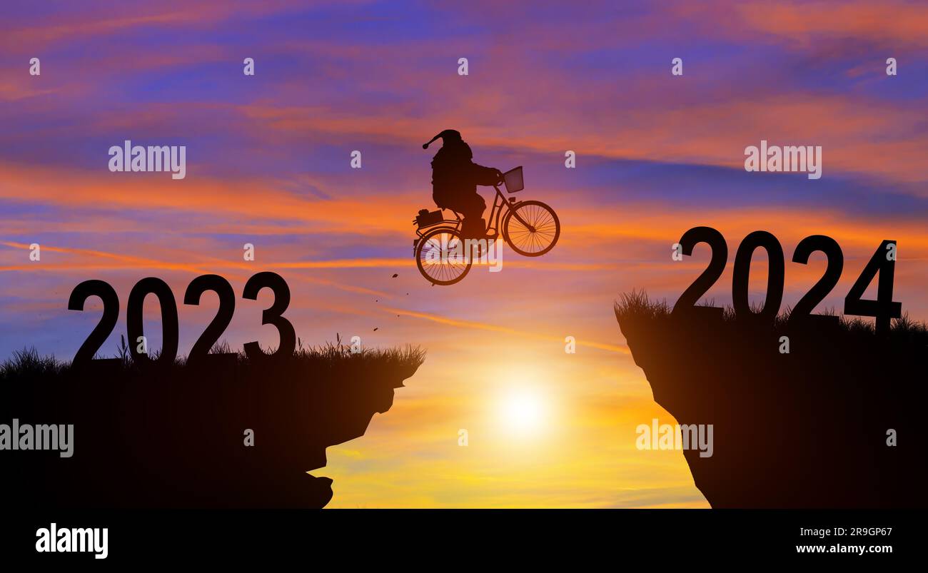 Welcome merry Christmas and Happy new year in 2024. Silhouette Santa Claus jumping across the gap with a bike from 2023 to 2024 cliff with Sunset. Stock Photo