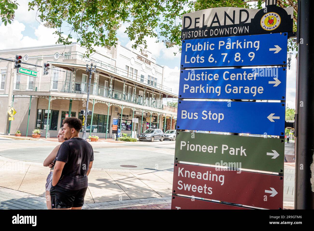 DeLand Florida,small town main street city historic downtown shopping district restored buildings,directional sign arrows information,couple crossing Stock Photo