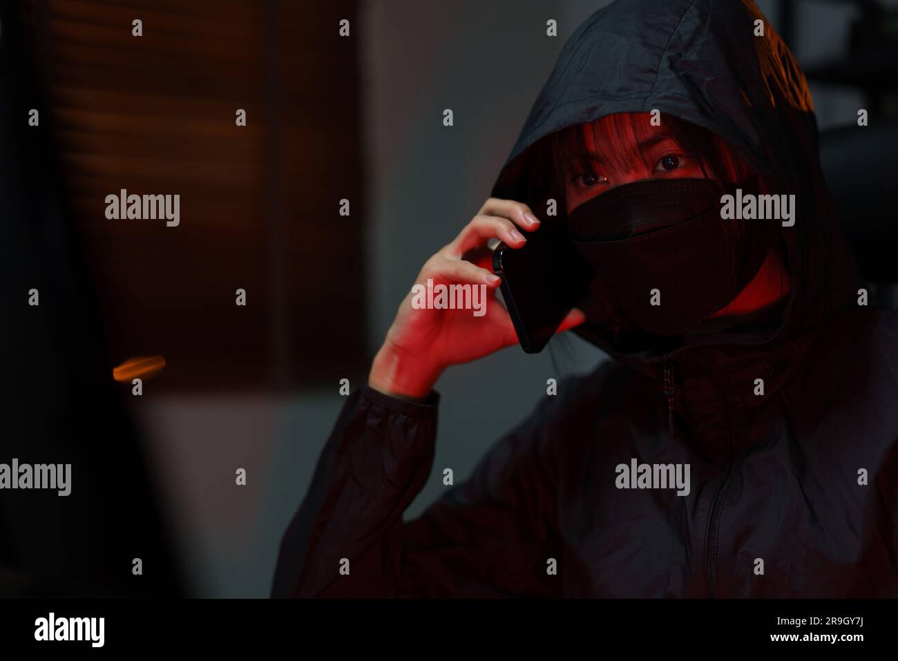 Hacker in hoodie talking on smartphone and typing code to hacking programming system or server. Stock Photo