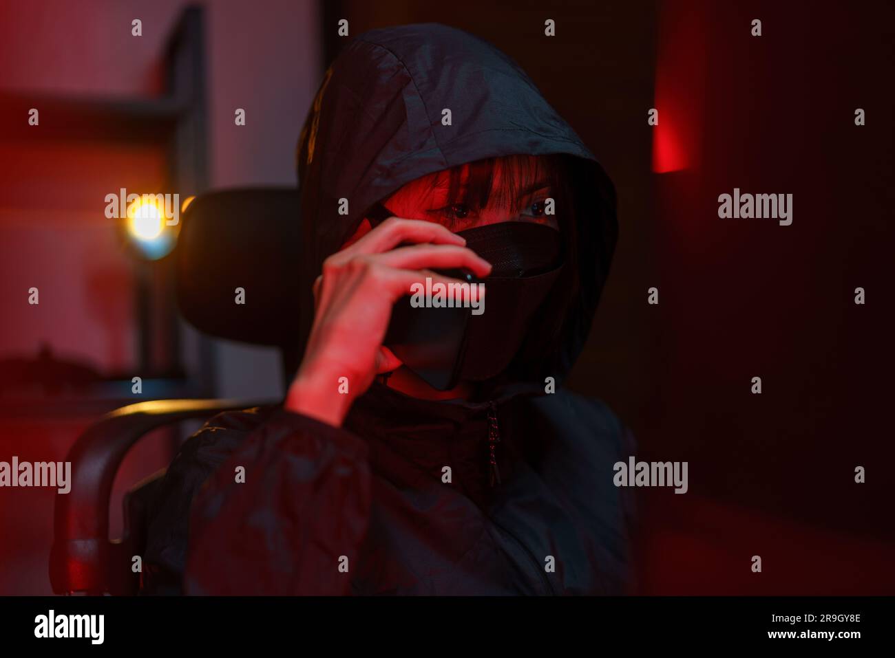 Hacker in hoodie talking on smartphone and typing code to hacking programming system or server. Stock Photo