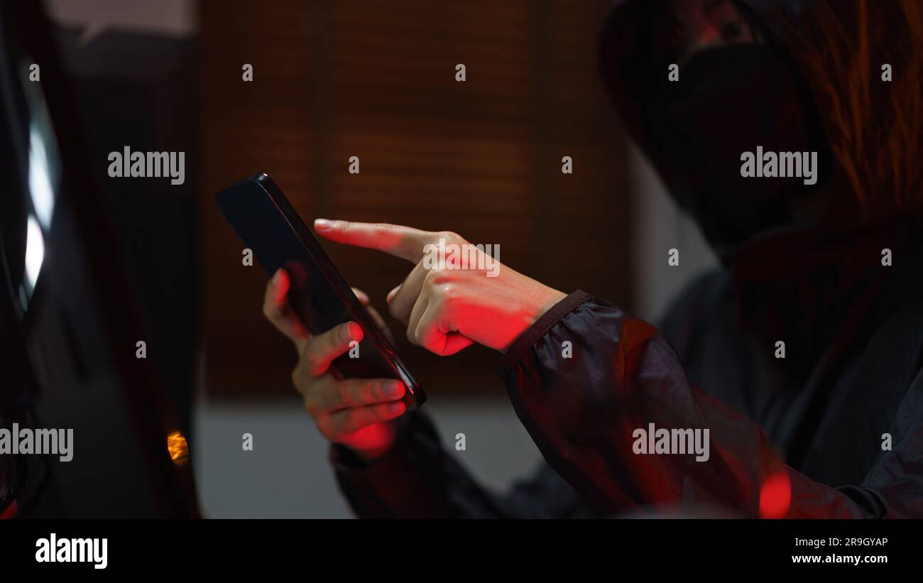 Hacker in hoodie using smartphone and computer to hacking programming system or data of server. Stock Photo