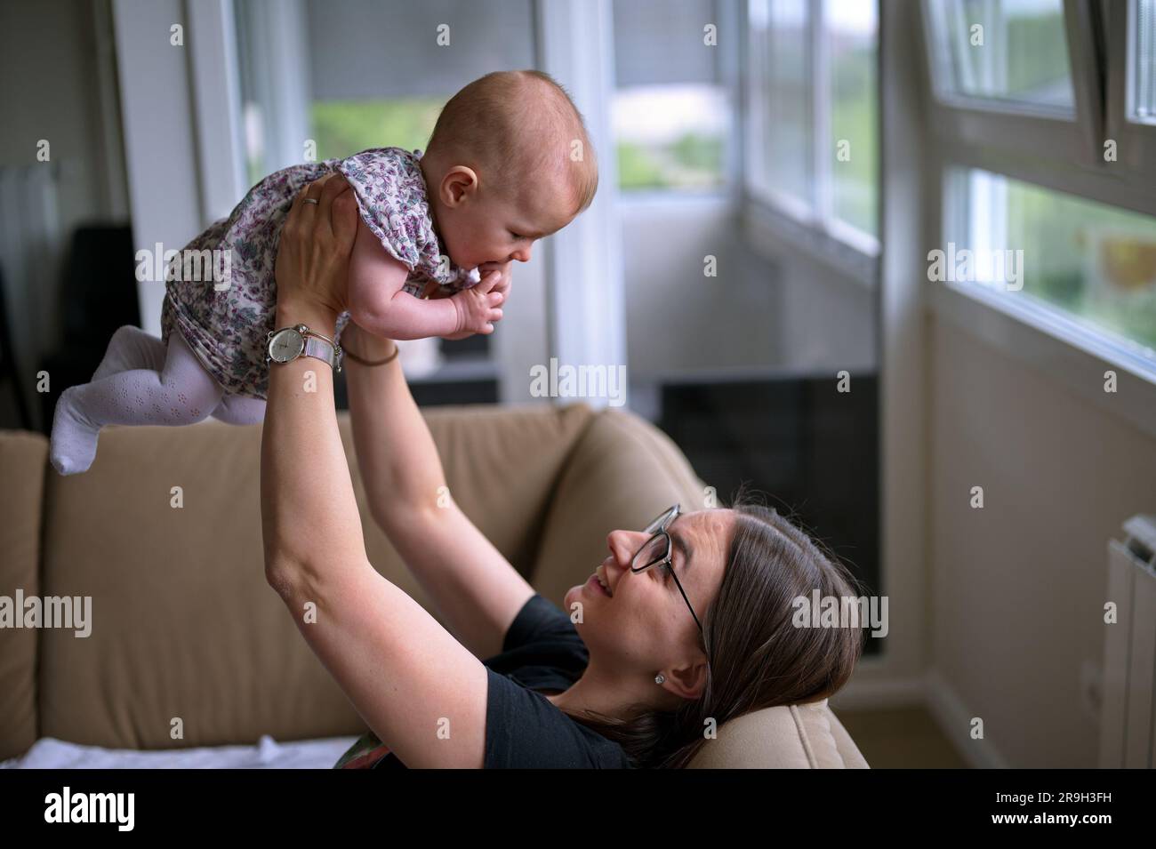 Mother sitting on a sofa and playing with cute little baby girl Stock Photo