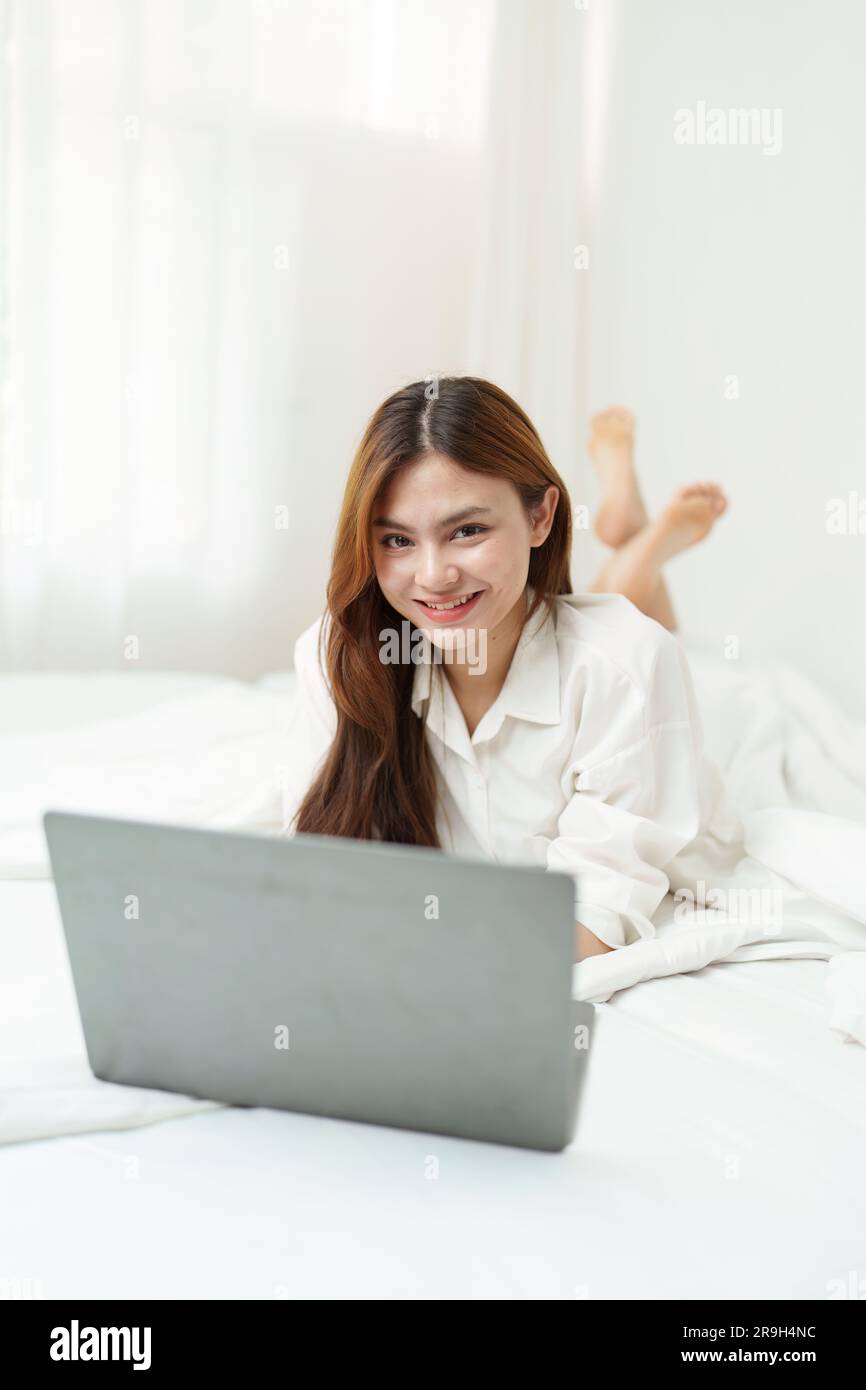 Happy smiling asian woman stretching on bed in the morning and using ...