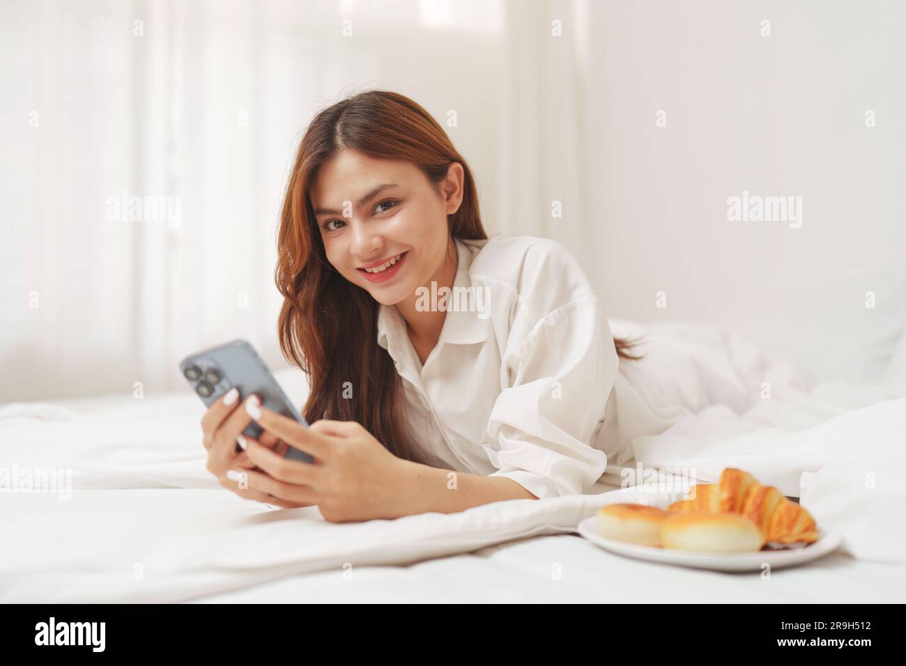 Happy smiling asian woman stretching on bed in the morning and holding ...