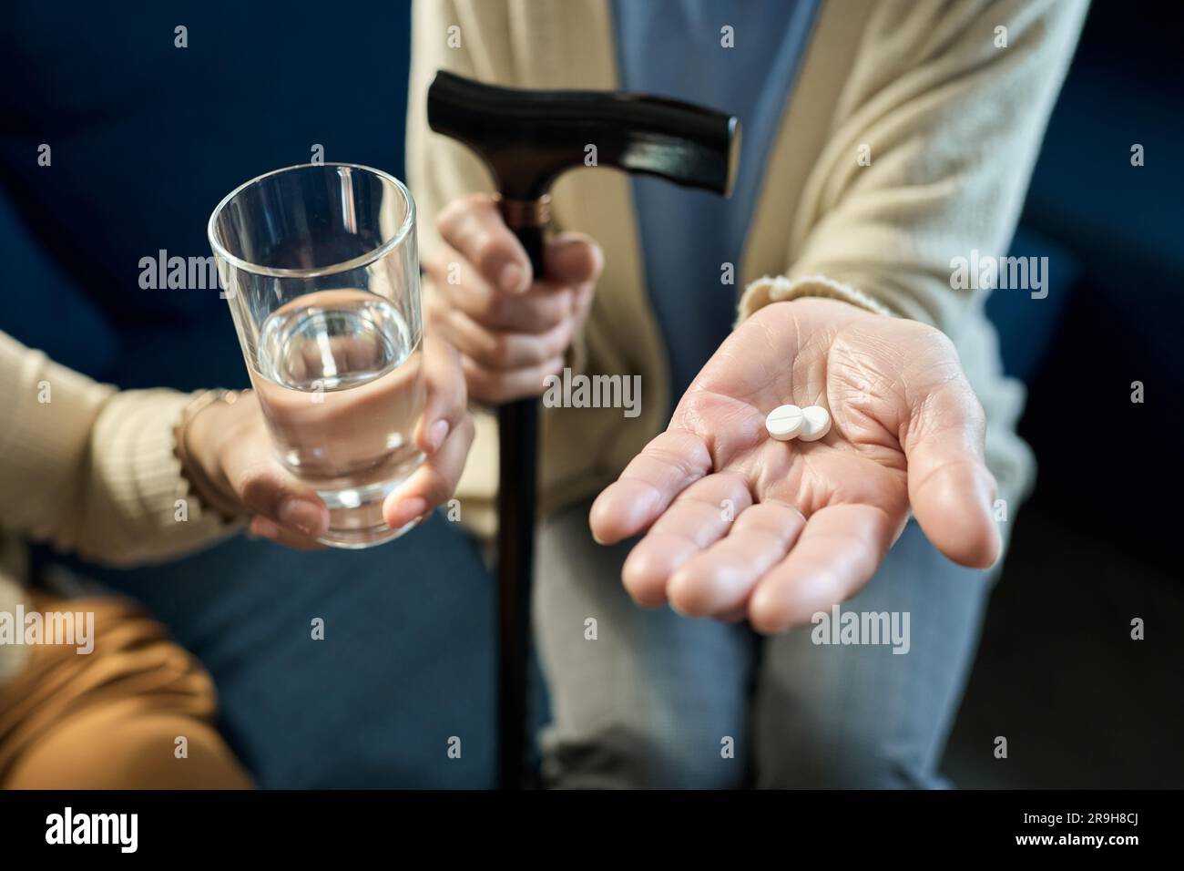Foocus on two pills on palm of senior woman and hand of her granddaughter passing glass of water while taking care of her grandma Stock Photo