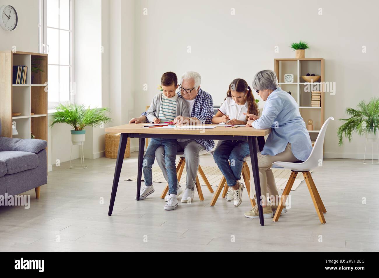Senior couple grandparents spending time with grandchildren at home drawing at table. Stock Photo
