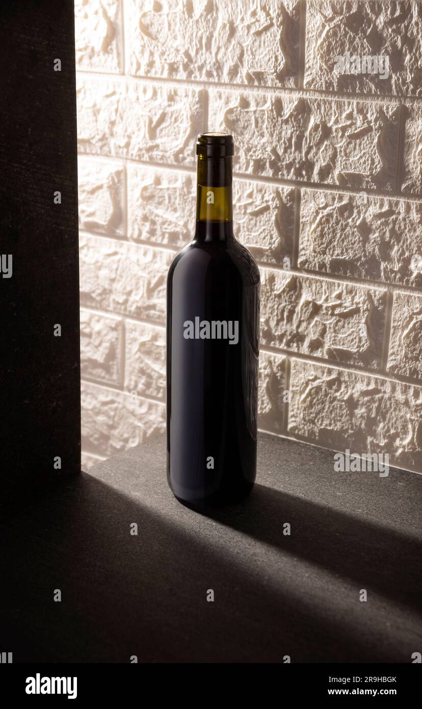Unlabeled red wine bottle mockup on gray stone surface, white rustic brick wall background. Diagonal long shadows. Minimalist concept. Stock Photo