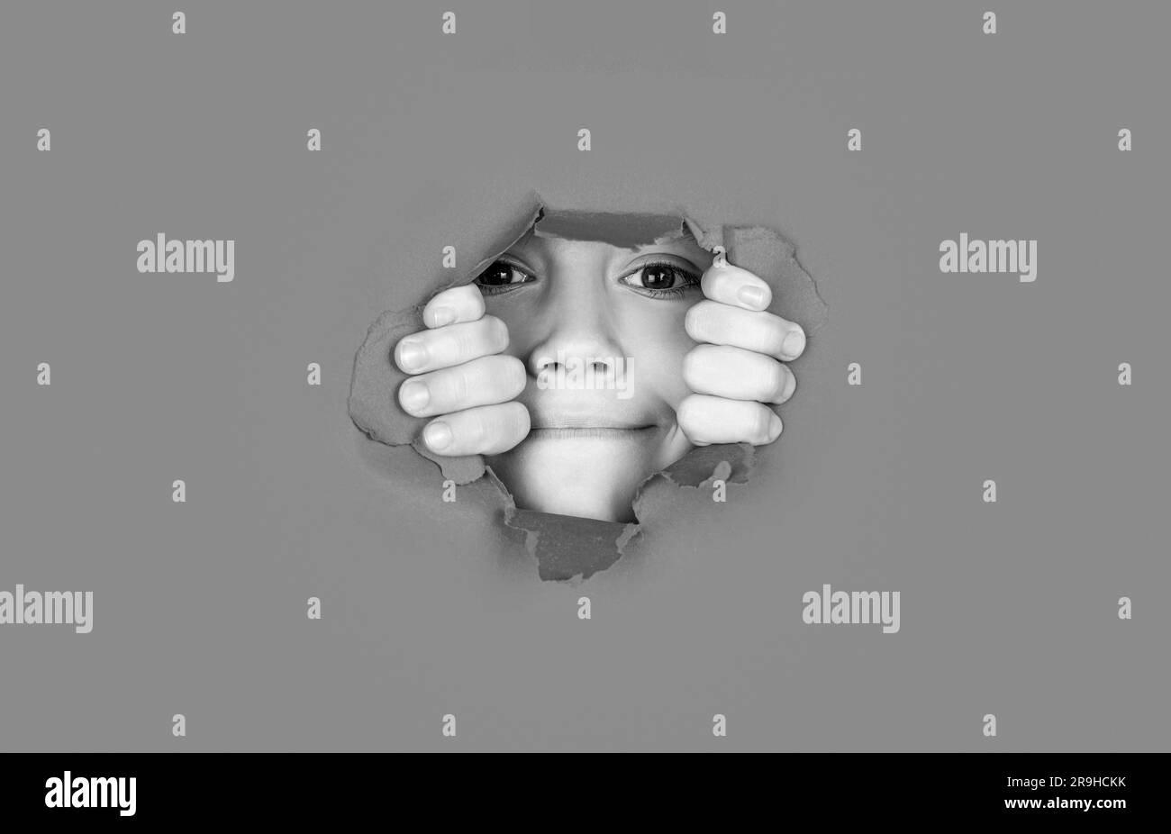 Kid with toothy smile shows face in paper hole. Positive child with