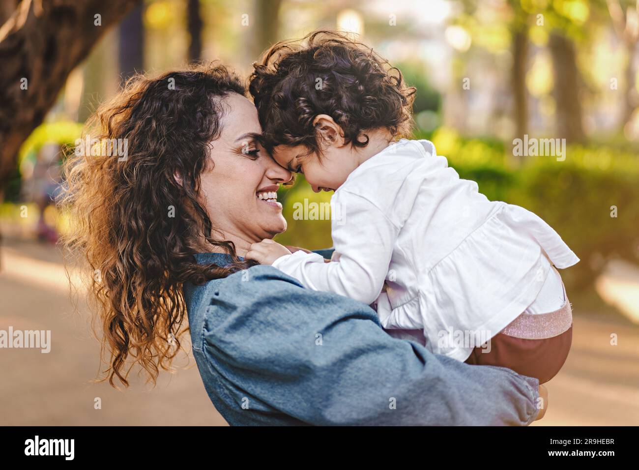 A light-brown curly-haired mother holds her 3-year-old daughter, their ...