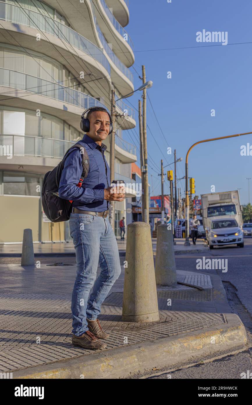 Young latin man with headphones and casual clothing crossing the street in a city. Stock Photo