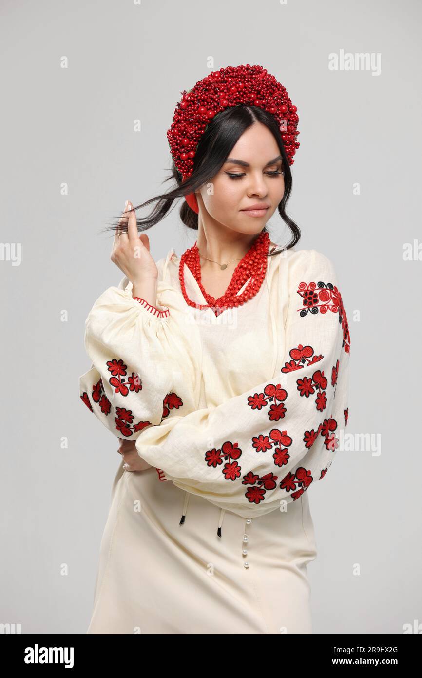 Vyshyvanka day in Ukraine. Beautiful young brunette woman dressed in Ukrainian traditional ethnic embroidered shirt, vyshyvanka, red wreath and necklaces at studio. Independence day, folk concept Stock Photo