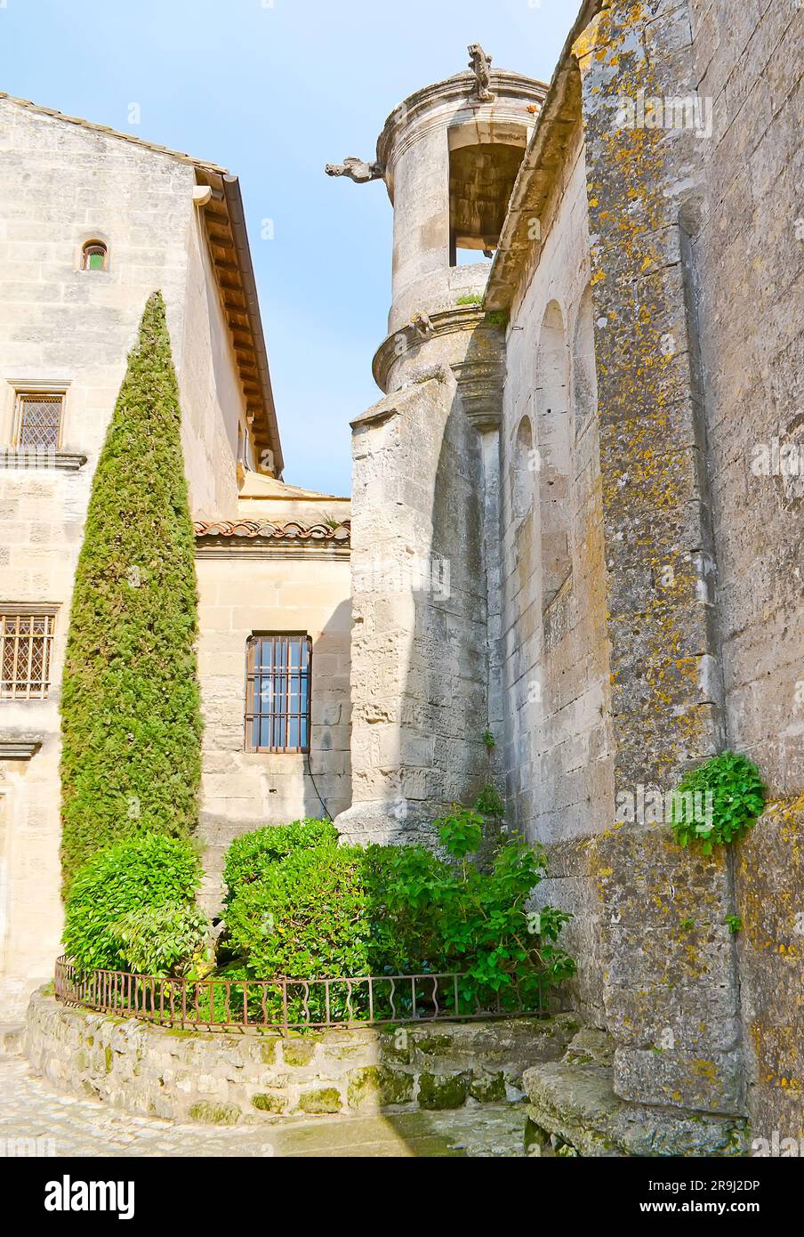 The medieval stone town of Les Baux-de-Provence with a corner and a tower of St Vincent Church and tiny flower bed with green plants and thuja tree, F Stock Photo