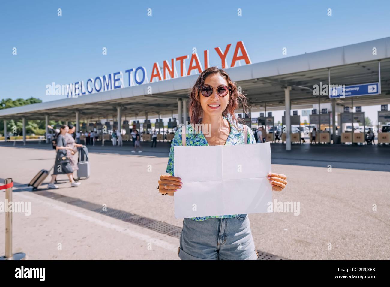Girl with blank paper at the welcome to Antalya sign at the arrival international terminal of Airport with tourists. Huge tourist traffic concept Stock Photo