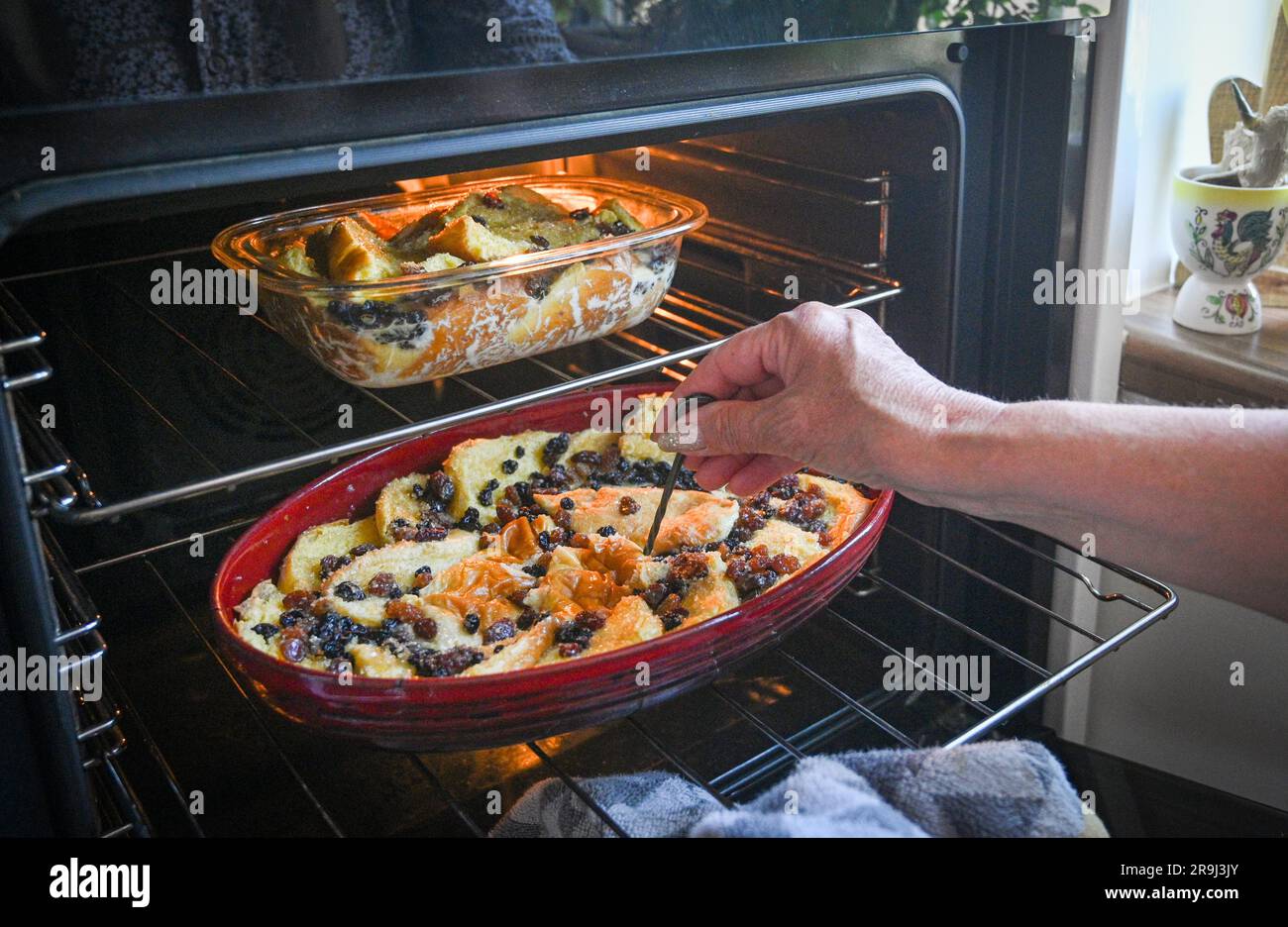 Home made bread and butter pudding being cooked in an electric fan oven in the kitchen and testing it is cooked fully with a skewer Stock Photo