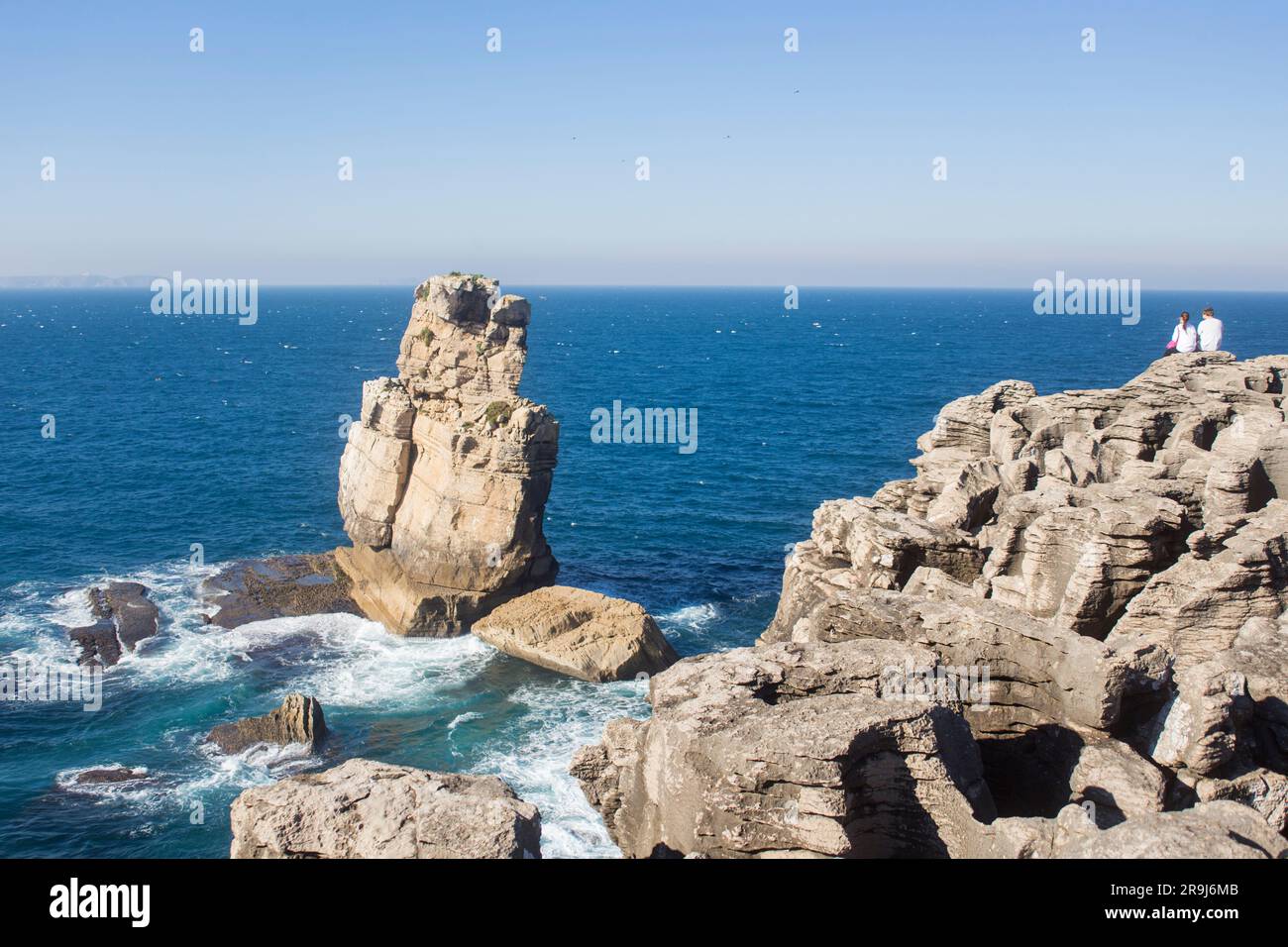 couple sitting on the cliff edge watching the beautiful blue sea Cabo Carvoeiro Peniche Portugal peniche; portugal Stock Photo