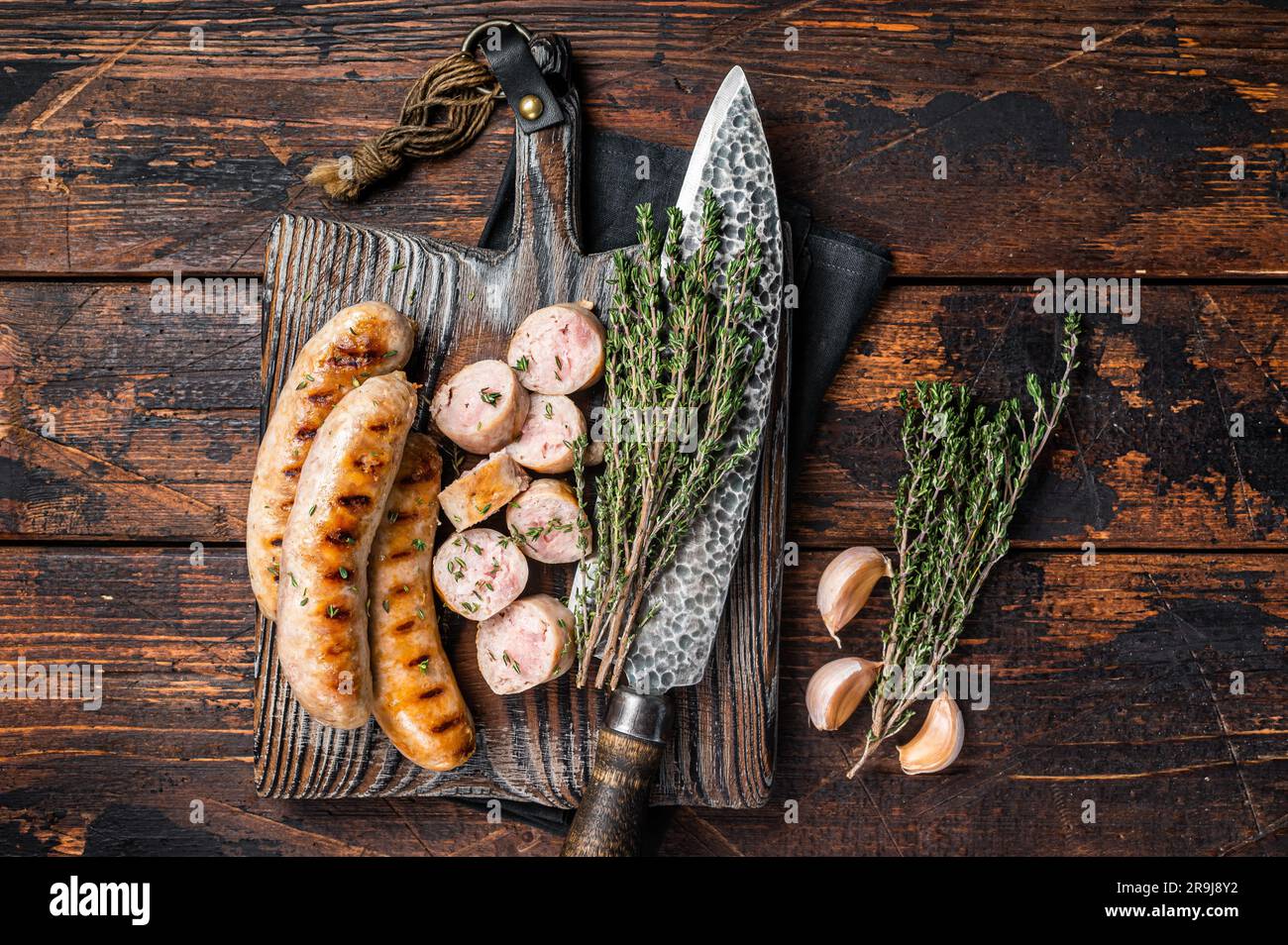 Sliced grilled pork meat sausages on a wooden serving board. Wooden background. Top view. Stock Photo