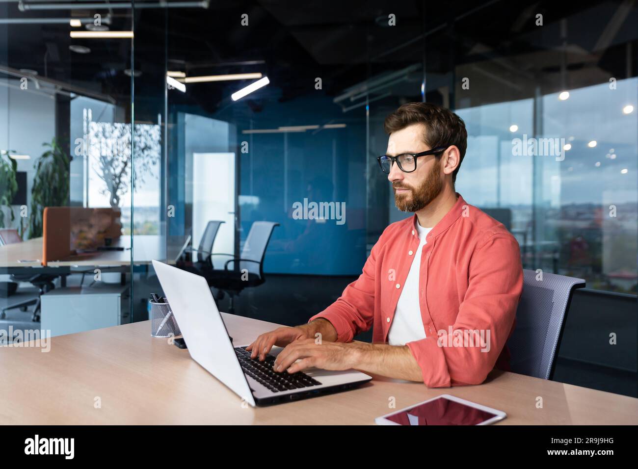 Thinking and serious man working with laptop inside office, focused programmer coding new software. Stock Photo