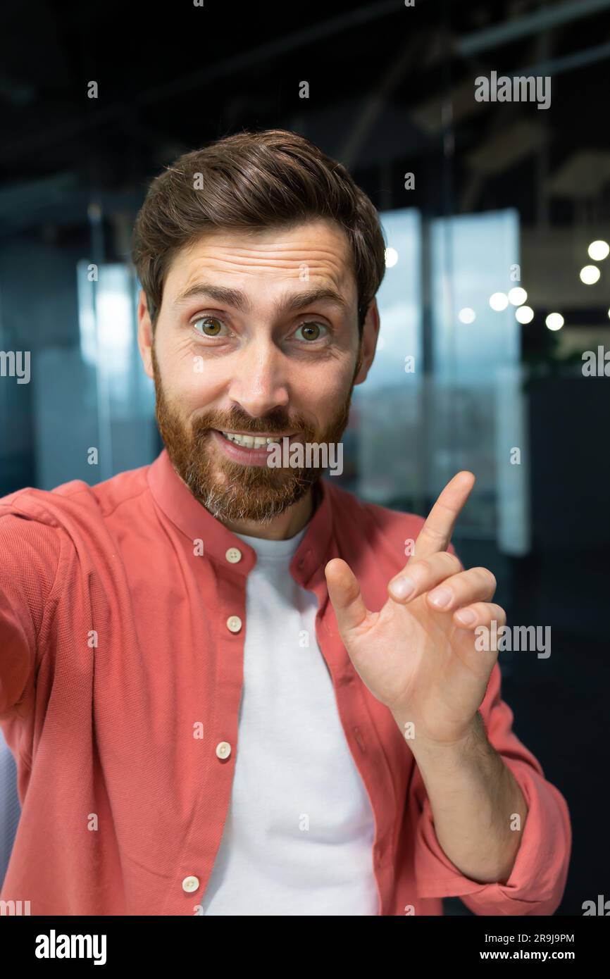 A businessman looks into the camera of the phone, pov. man inside office talking with friends smiling using app on smartphone for video call. Vertical shot Stock Photo