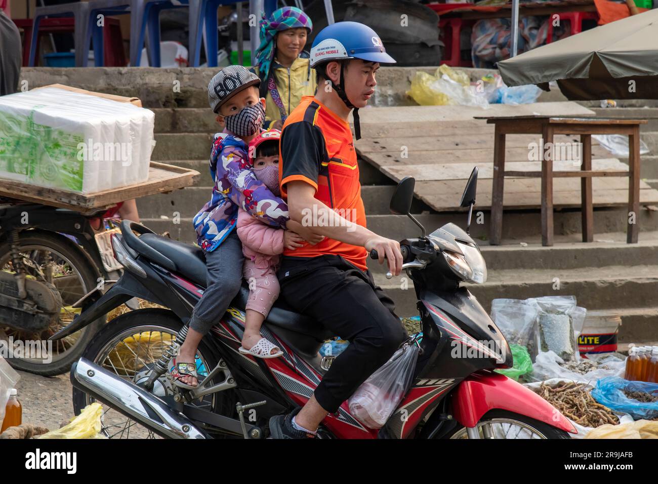 Bac Ha, Vietnam-April 2023; Close up of a young man on a scooter together with young children holding on tightly to the father on the Bac Ha Sunday ma Stock Photo