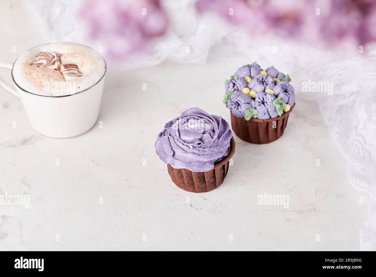 Floral delicate french purple cupcakes using trend Dreamy Escapism. Aesthetics desserts, coffee cup and lilac flowers background Stock Photo