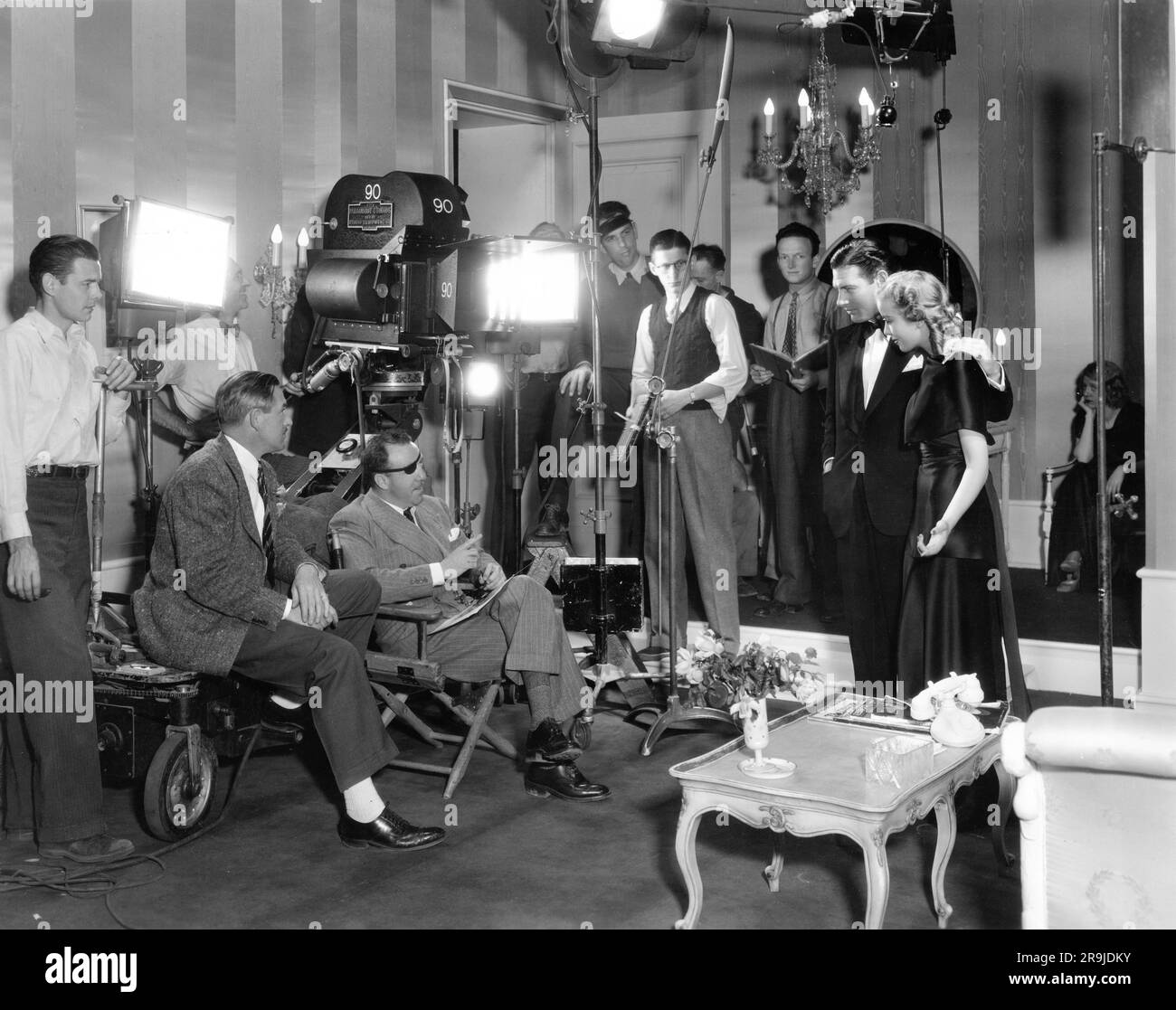 Director RAOUL WALSH and Movie Crew on set candid with RICHARD ARLEN and IDA LUPINO during filming of ARTISTS AND MODELS 1937 director RAOUL WALSH cinematographer Victor Milner costumes Travis Banton Paramount Pictures Stock Photo