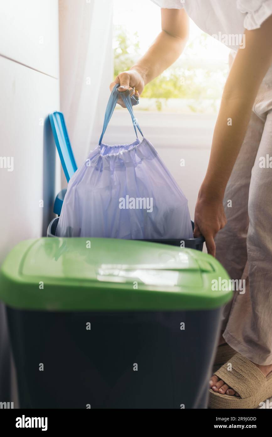 Side view of anonymous crop woman taking out garbage bag from a container near window in kitchen against blurred background Stock Photo