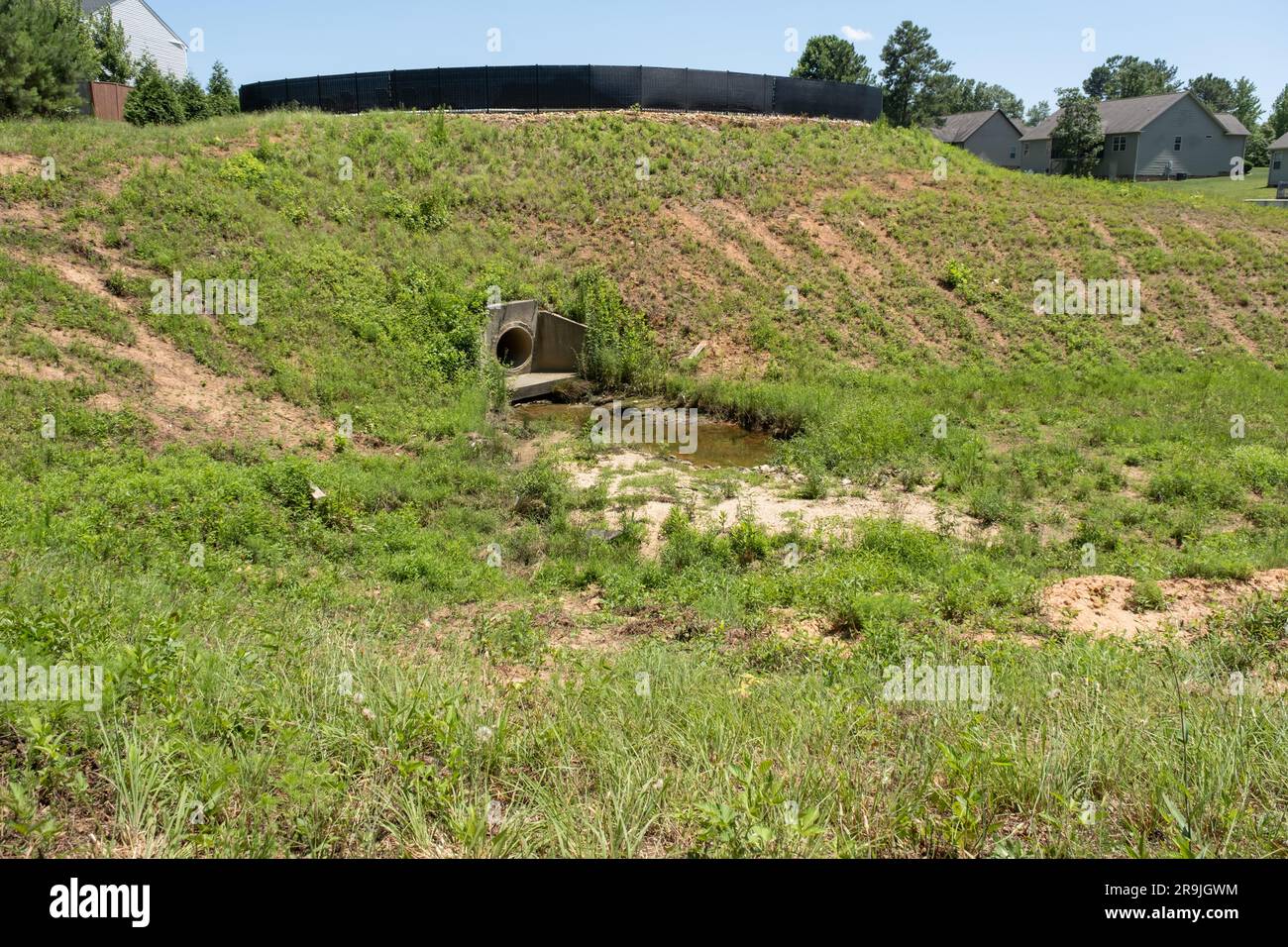 Large drainage ditch lined with grass and weeds behind a subdivision Stock Photo