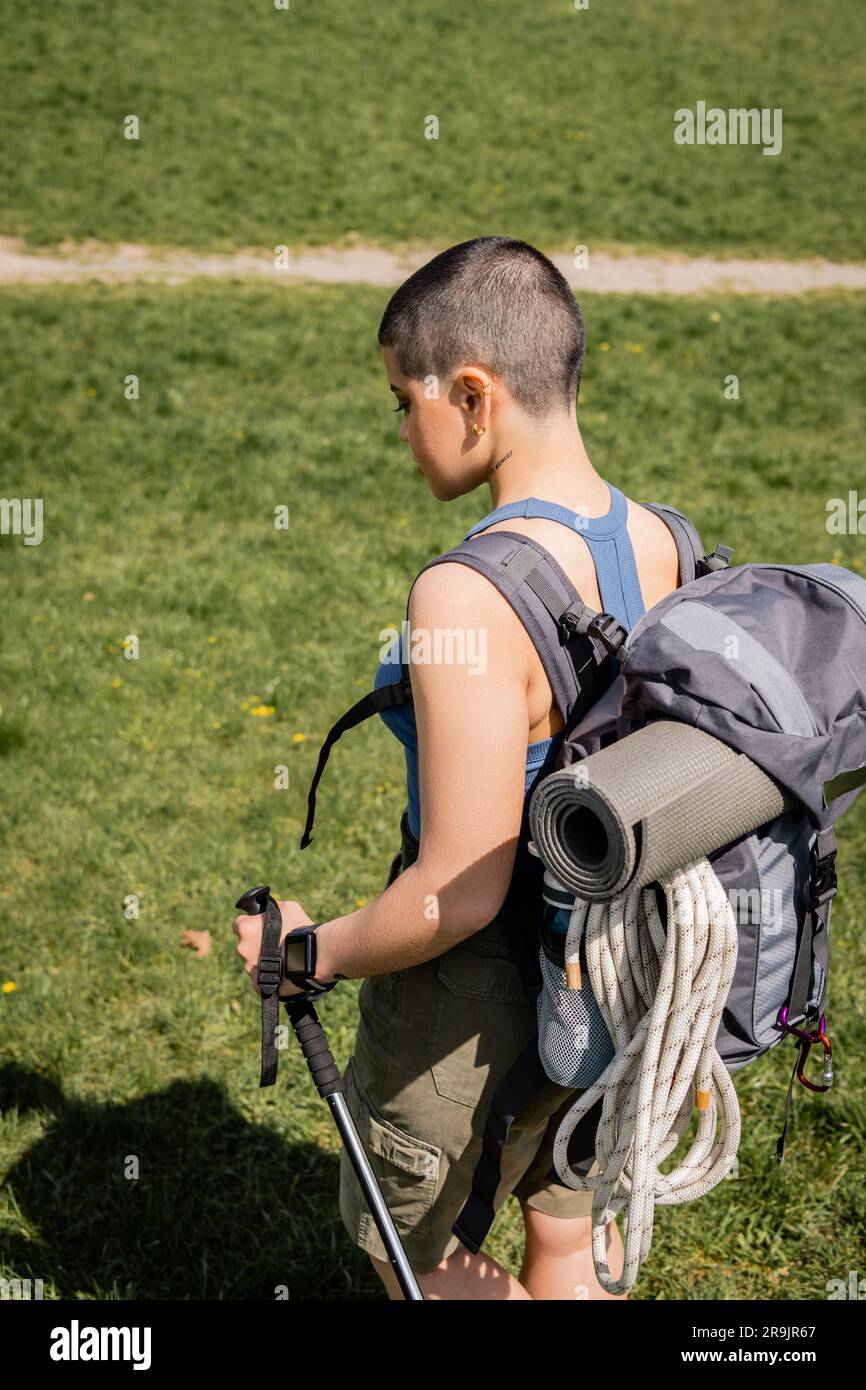 Side view of young short haired and tattooed female hiker with backpack ...