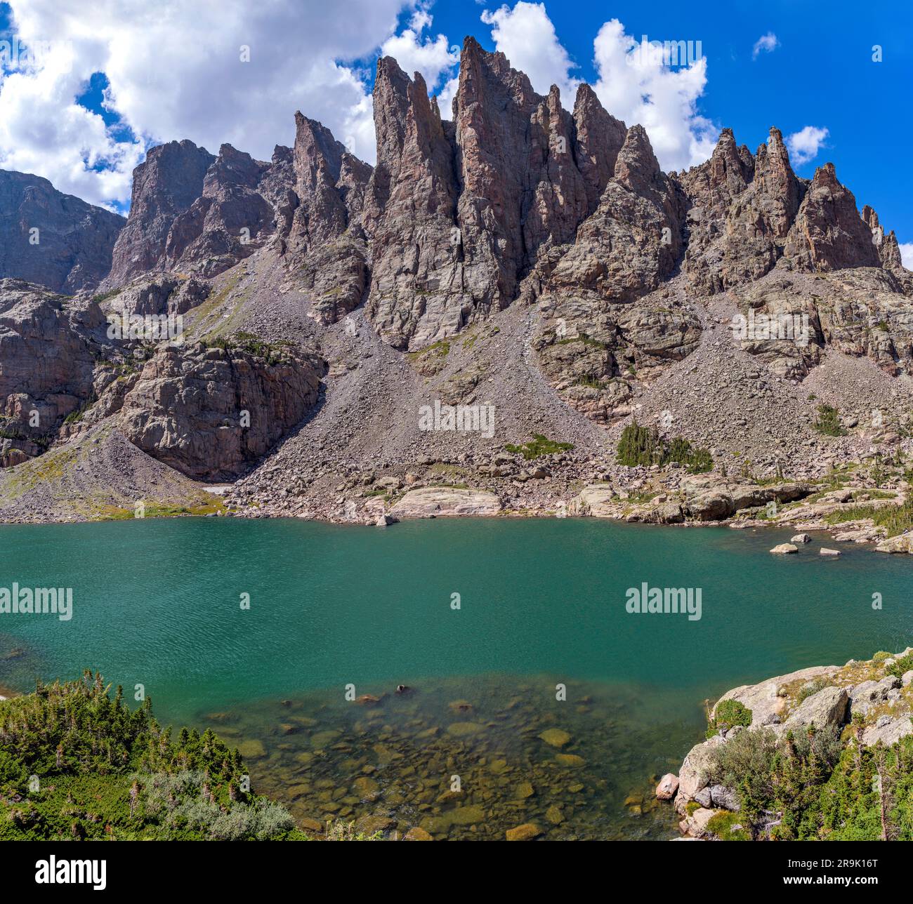 Sky Pond and Sharkstooth - A sunny Summer day view of clear and colorful Sky Pond, with rugged pinnacles of Sharkstooth towering at shore. RMNP, CO. Stock Photo