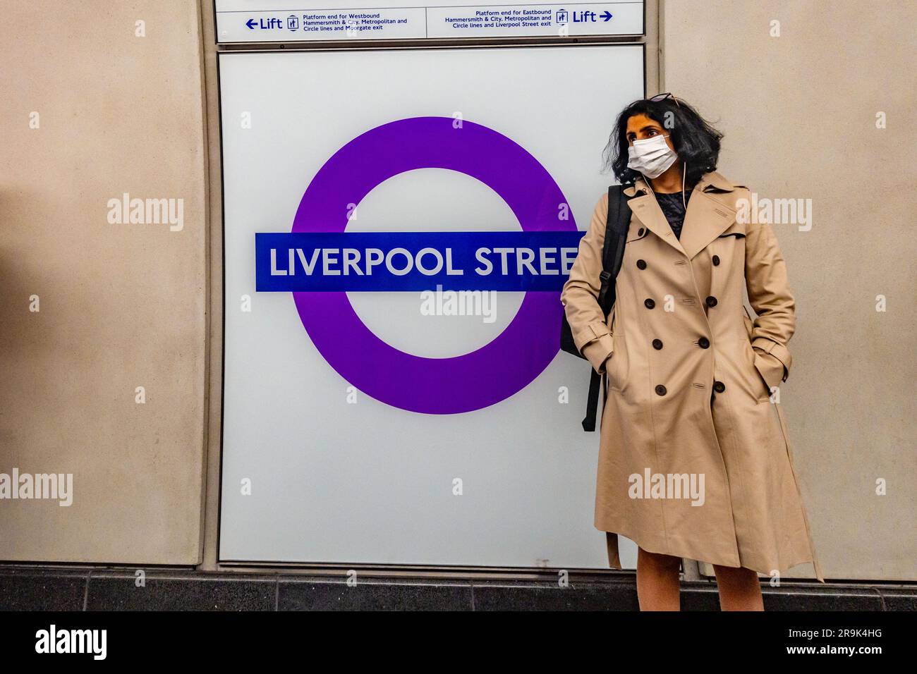 A lady wearing a face mask stands next to a Liverpool Street Elizabeth Line sign at Liverpool Street London Underground station Stock Photo