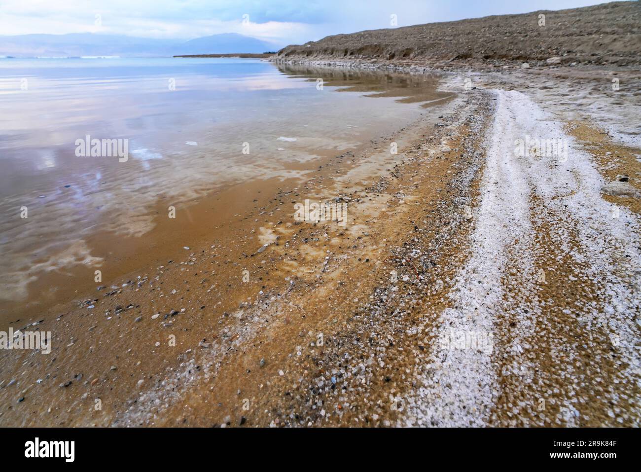 Sand covered with crystalline salt on shore of Dead Sea, calm clear water near - typical scenery at Ein Bokek beach, Israel Stock Photo