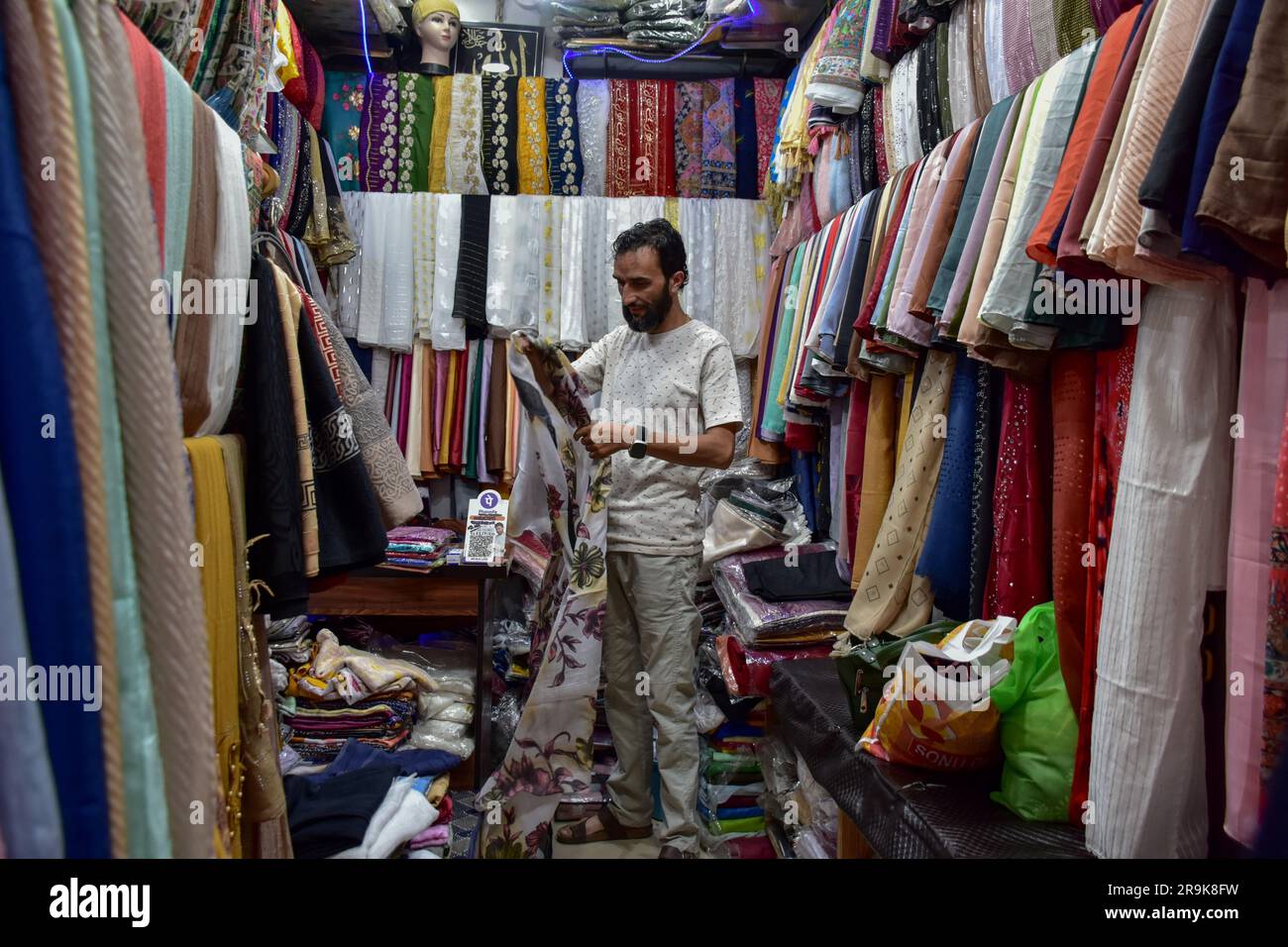 Srinagar, India. 27th June, 2023. A salesman sorts clothes inside his shop  ahead of the ahead of the Eid al-Adha at a local market. Markets witness a  huge shopping rush in preparation