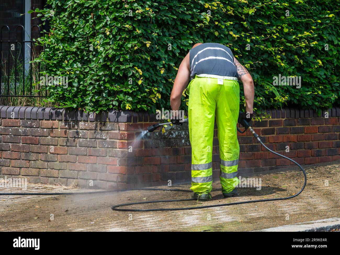 Man pressure washing a wall outside in Summer, with a hose and pressure washer, UK. Stock Photo