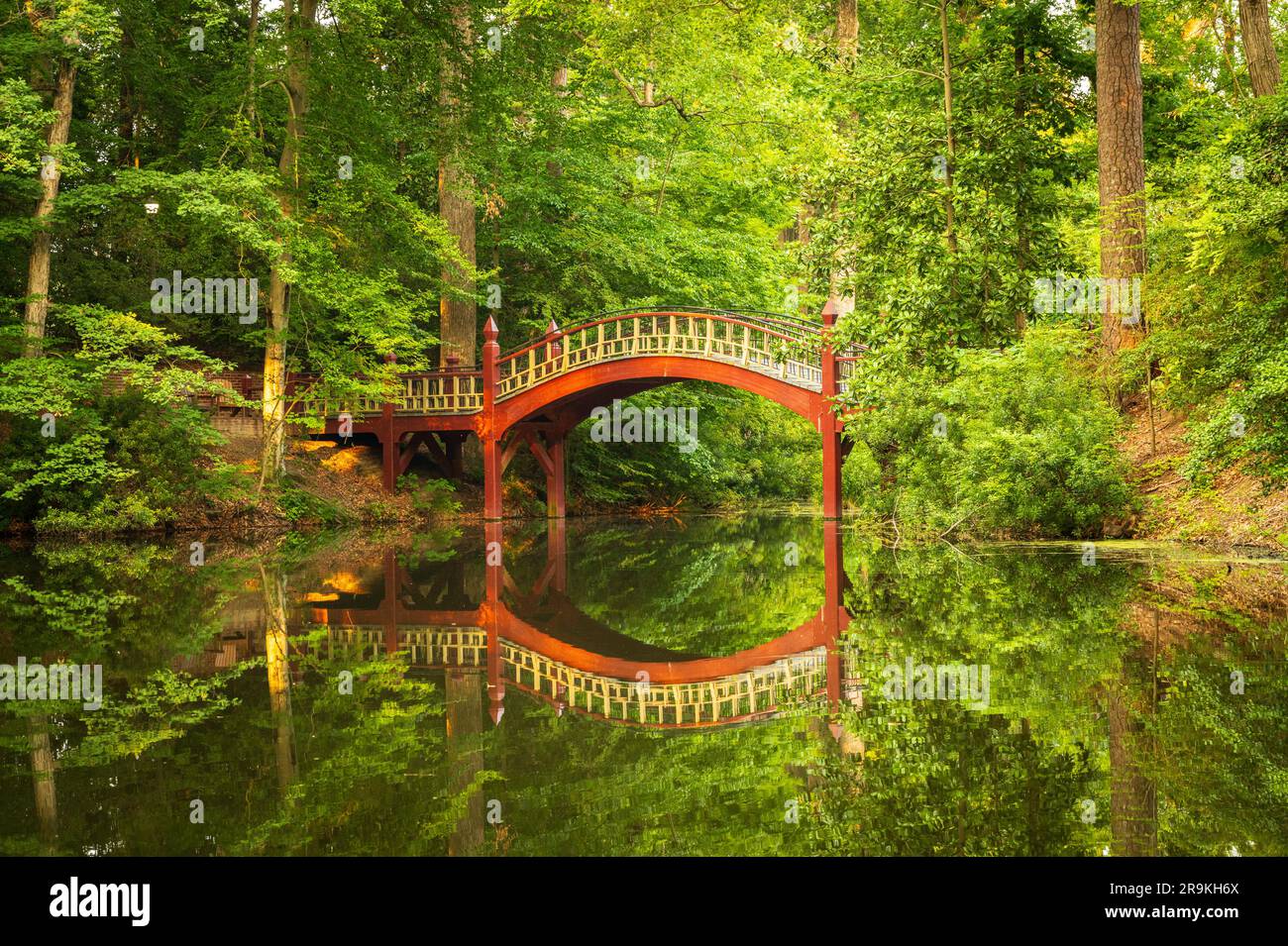Ornate wooden bridge over very calm Crim Dell pond on campus of William and Mary college in Williamsburg Virginia Stock Photo